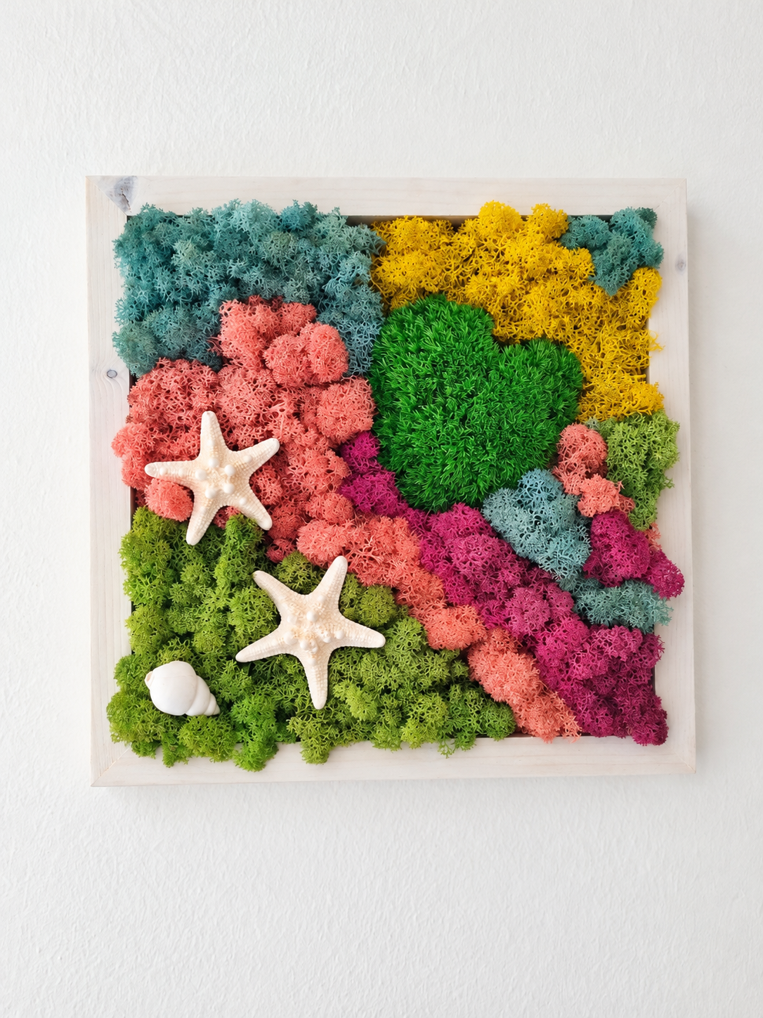 Dettaglio di quadro vegetale artigianale con muschio stabilizzato nei toni del verde, rosa, giallo e azzurro, cuore verde centrale e decorazioni marine.